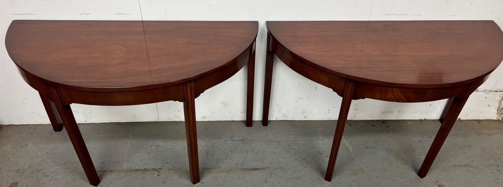 A pair of semi-circular George IV mahogany demilune console tables with polished surfaces and straight tapered legs.