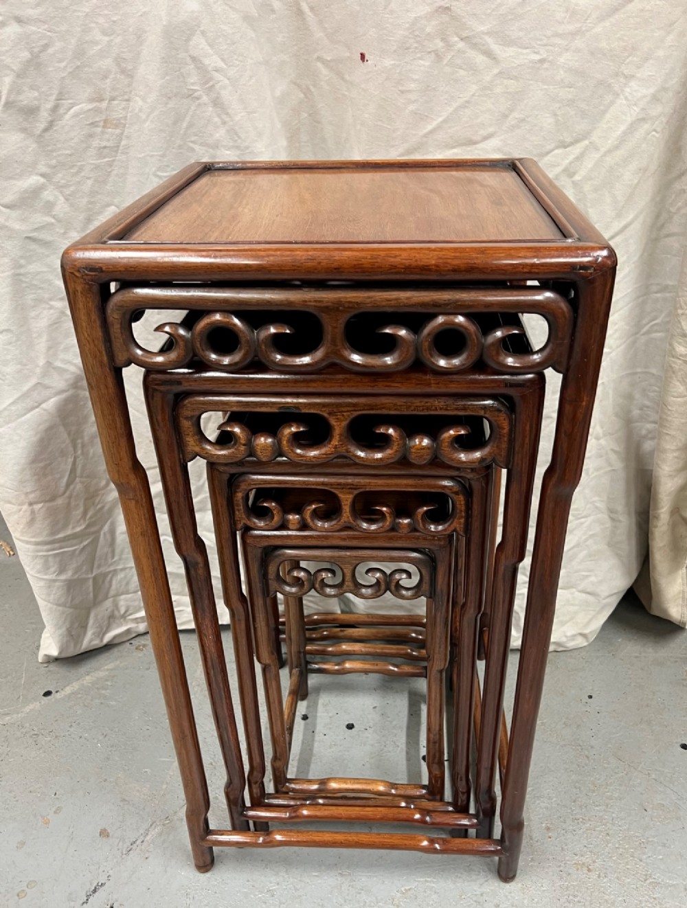 A set of four graduated brown Chinese hardwood nesting tables featuring carved scroll aprons and floating panel tops. View III