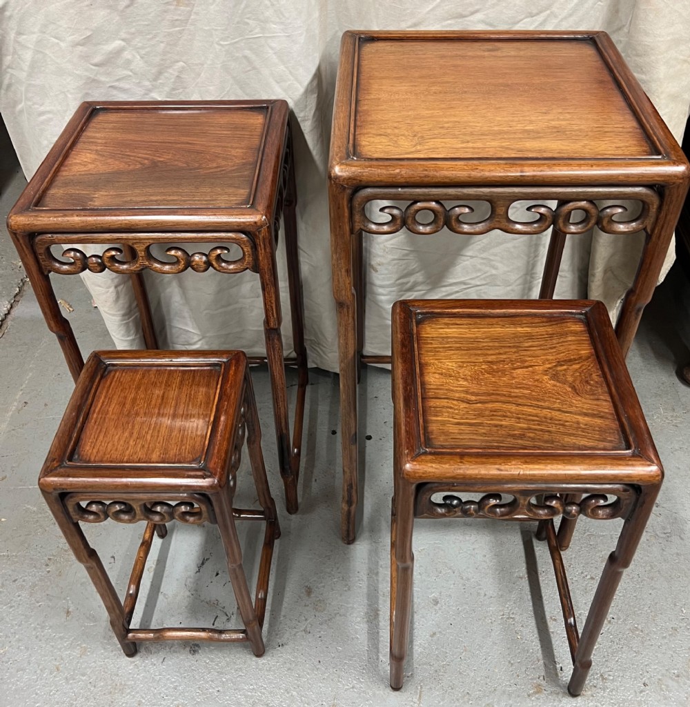 A set of four graduated brown Chinese hardwood nesting tables featuring carved scroll aprons and floating panel tops. View IV
