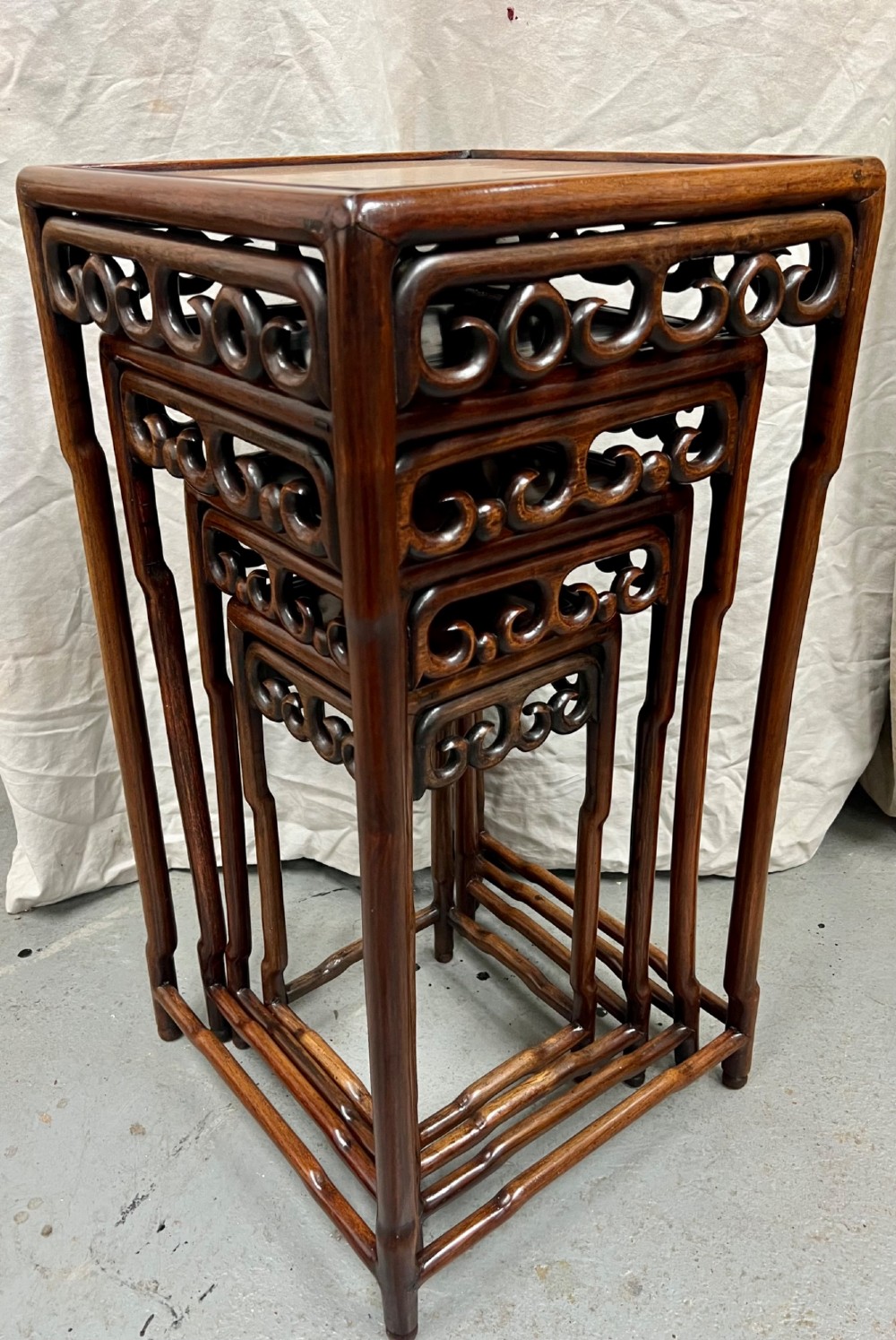 A set of four graduated brown Chinese hardwood nesting tables featuring carved scroll aprons and floating panel tops. View IX