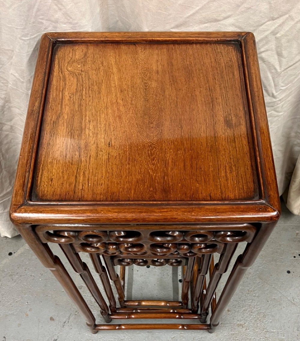 A set of four graduated brown Chinese hardwood nesting tables featuring carved scroll aprons and floating panel tops. View X