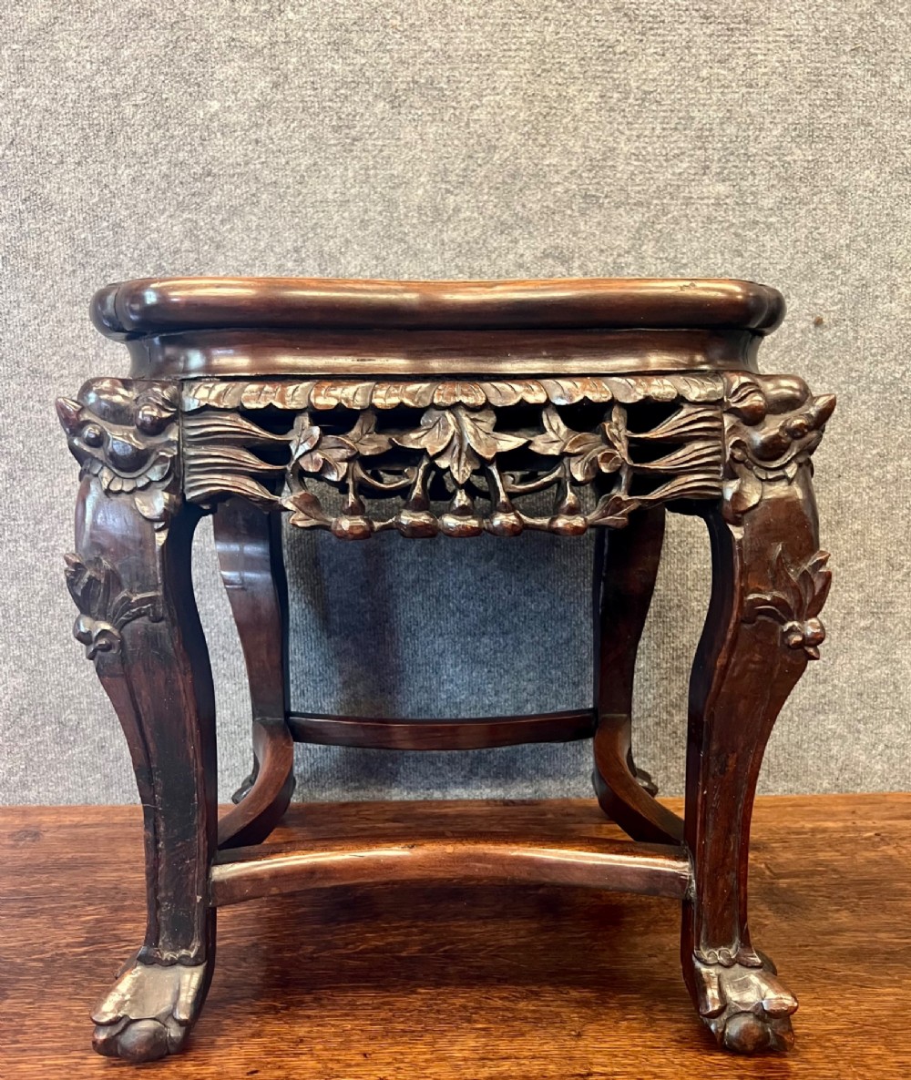 A dark carved Chinese hardwood stand featuring a pierced foliage apron, cabriole legs with mask details, and low stretchers.