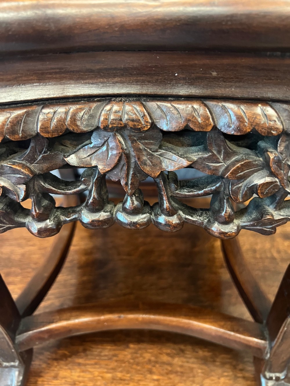 A dark carved Chinese hardwood stand featuring a pierced foliage apron, cabriole legs with mask details, and low stretchers. View V
