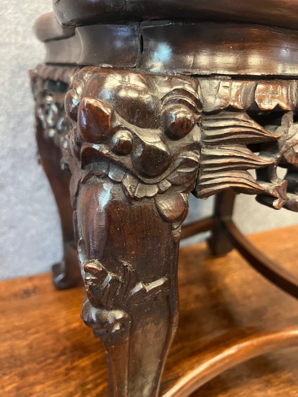 A dark carved Chinese hardwood stand featuring a pierced foliage apron, cabriole legs with mask details, and low stretchers. View VI