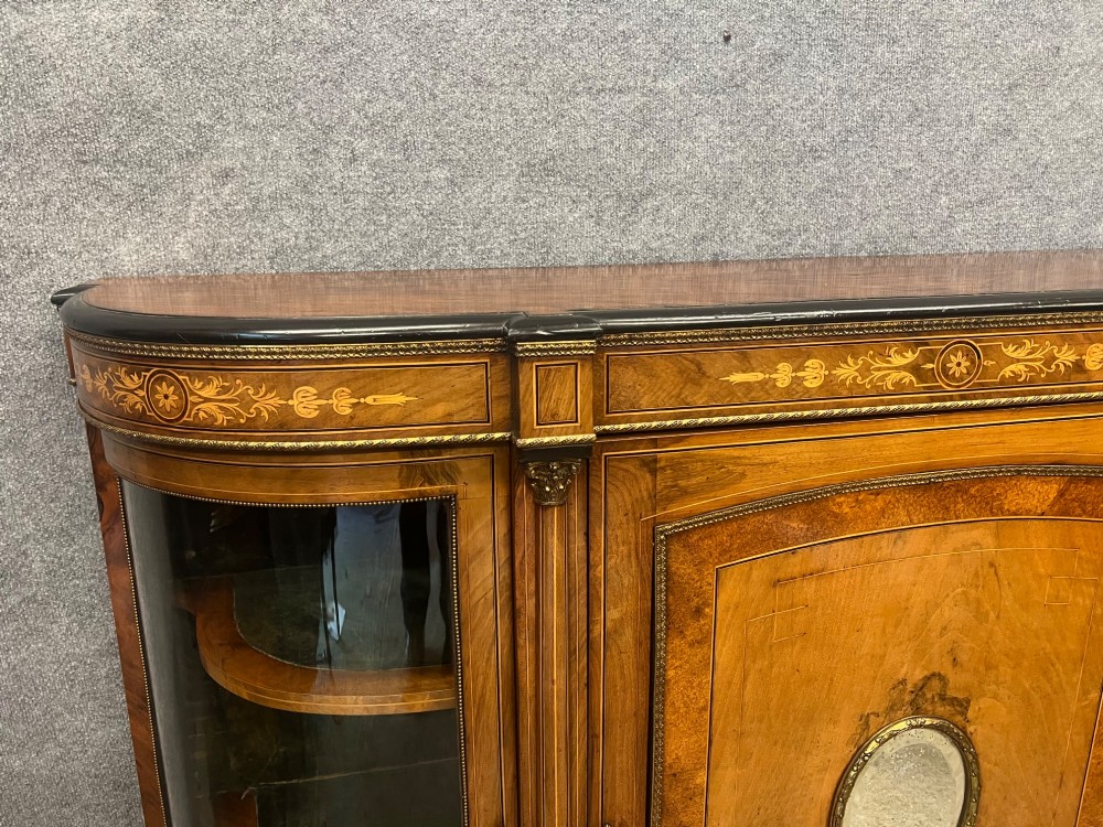 A Victorian credenza crafted from burr walnut with floral marquetry inlay, a central panelled cupboard door, curved glass display bays, and ornate ormolu mounts. View V