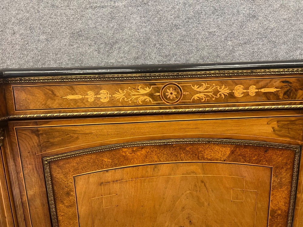A Victorian credenza crafted from burr walnut with floral marquetry inlay, a central panelled cupboard door, curved glass display bays, and ornate ormolu mounts. View VI