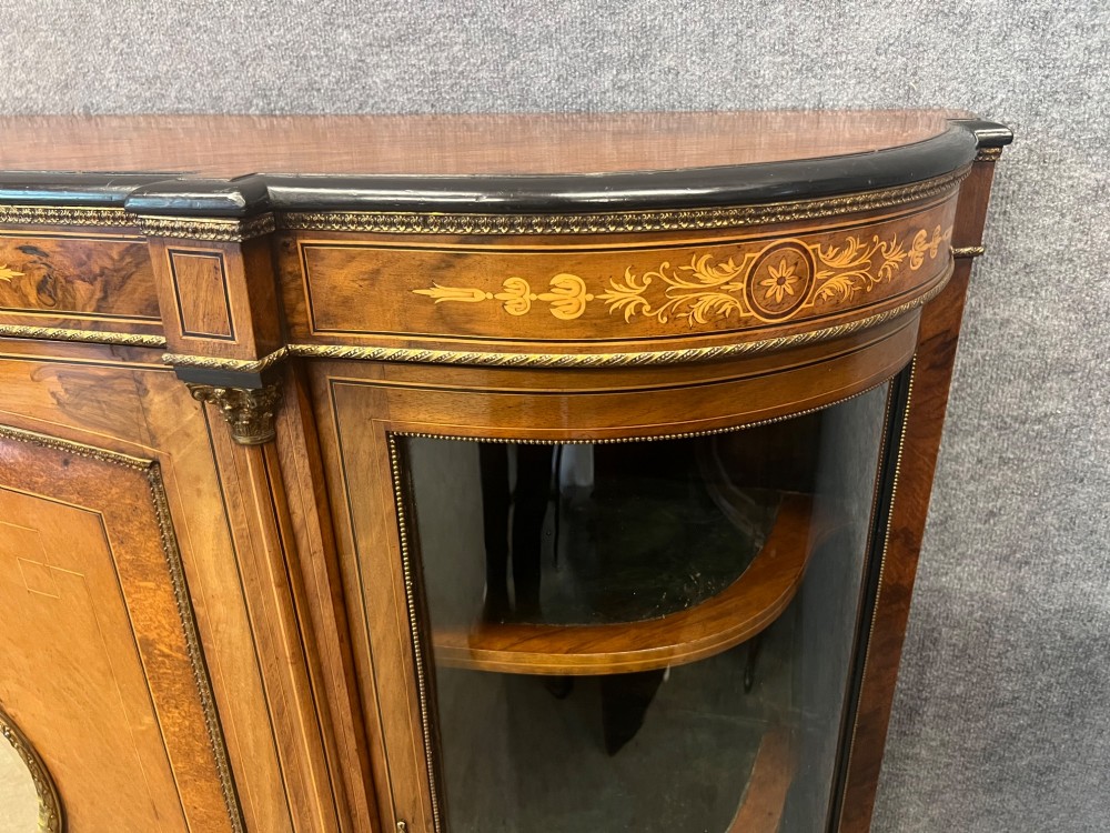 A Victorian credenza crafted from burr walnut with floral marquetry inlay, a central panelled cupboard door, curved glass display bays, and ornate ormolu mounts. View VII