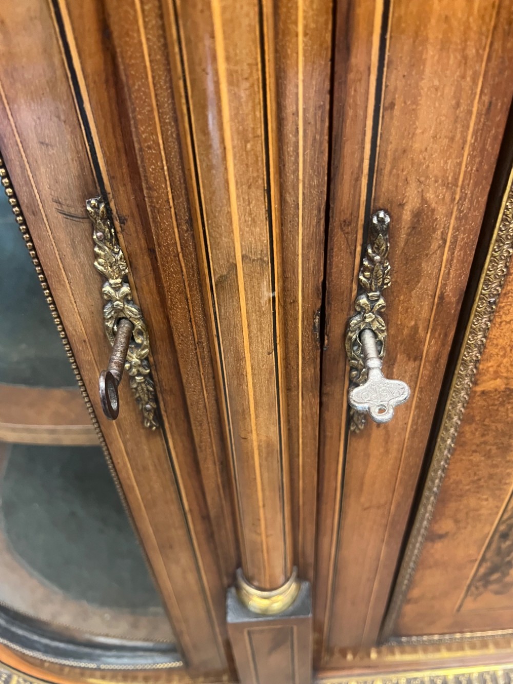 A Victorian credenza crafted from burr walnut with floral marquetry inlay, a central panelled cupboard door, curved glass display bays, and ornate ormolu mounts. View IX