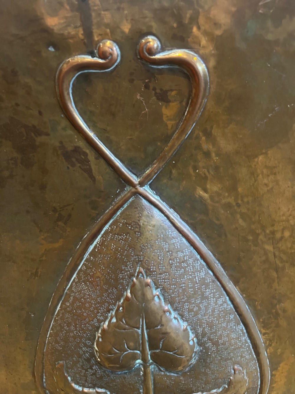 A rectangular hammered copper Arts and Crafts fire screen embossed with stylised botanical leaf motifs, set within a black wrought iron frame with scrolled legs and an arched carrying handle. View III