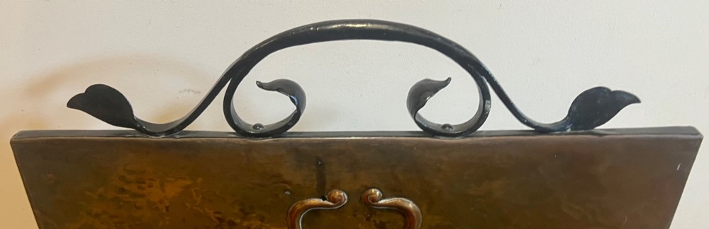 A rectangular hammered copper Arts and Crafts fire screen embossed with stylised botanical leaf motifs, set within a black wrought iron frame with scrolled legs and an arched carrying handle. View VII