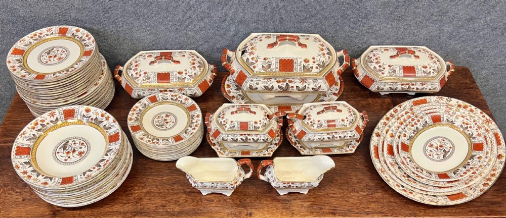 A fifty-nine piece Victorian earthenware dinner service decorated in rust orange, brown floral transfer patterns, and gilt accents arranged on a dark wood surface.