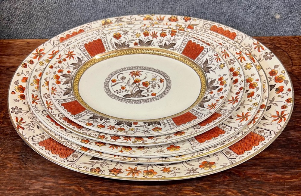 A fifty-nine piece Victorian earthenware dinner service decorated in rust orange, brown floral transfer patterns, and gilt accents arranged on a dark wood surface. View VII