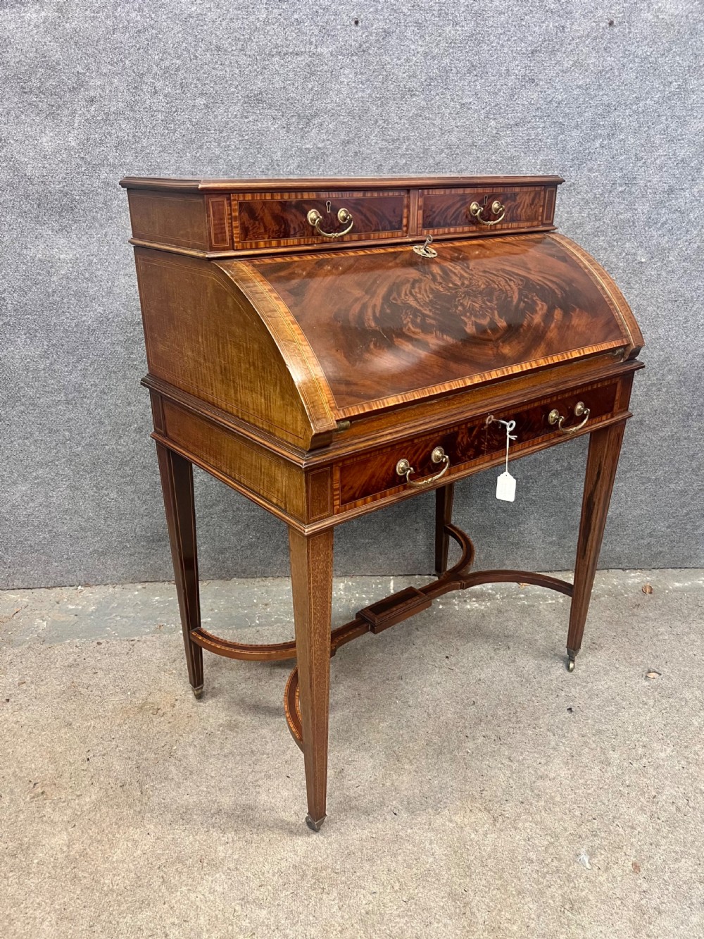 An Edwardian Sheraton Revival mahogany and satinwood cylinder ladies desk featuring crossbanded marquetry, brass drop handles, square tapered legs, and castors.
