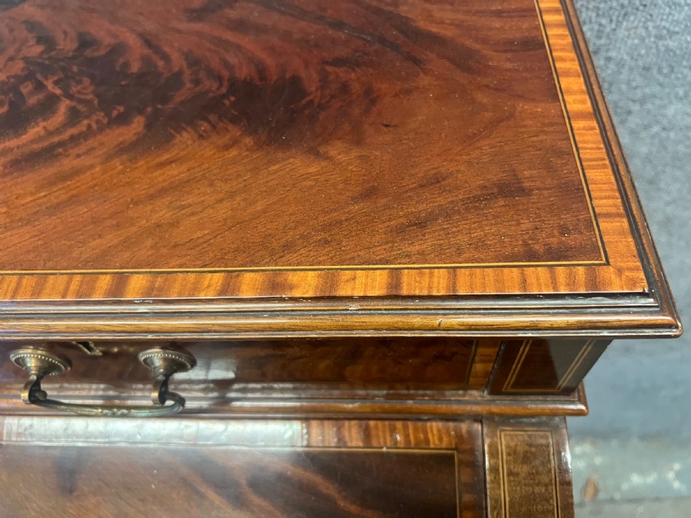 An Edwardian Sheraton Revival mahogany and satinwood cylinder ladies desk featuring crossbanded marquetry, brass drop handles, square tapered legs, and castors. View VI