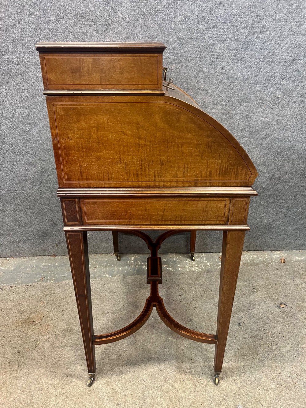 An Edwardian Sheraton Revival mahogany and satinwood cylinder ladies desk featuring crossbanded marquetry, brass drop handles, square tapered legs, and castors. View IX