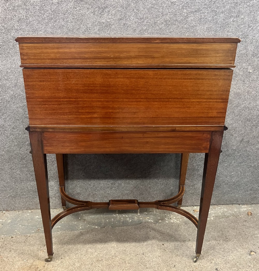 An Edwardian Sheraton Revival mahogany and satinwood cylinder ladies desk featuring crossbanded marquetry, brass drop handles, square tapered legs, and castors. View X