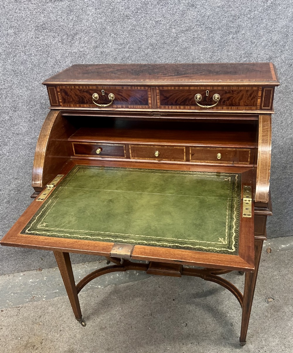An Edwardian Sheraton Revival mahogany and satinwood cylinder ladies desk featuring crossbanded marquetry, brass drop handles, square tapered legs, and castors. View XI