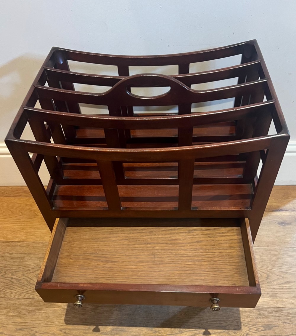 An Edwardian mahogany canterbury with four slatted compartments, a central cut-out handle, a single base drawer with brass knobs, and tapered legs on brass castors. View IV