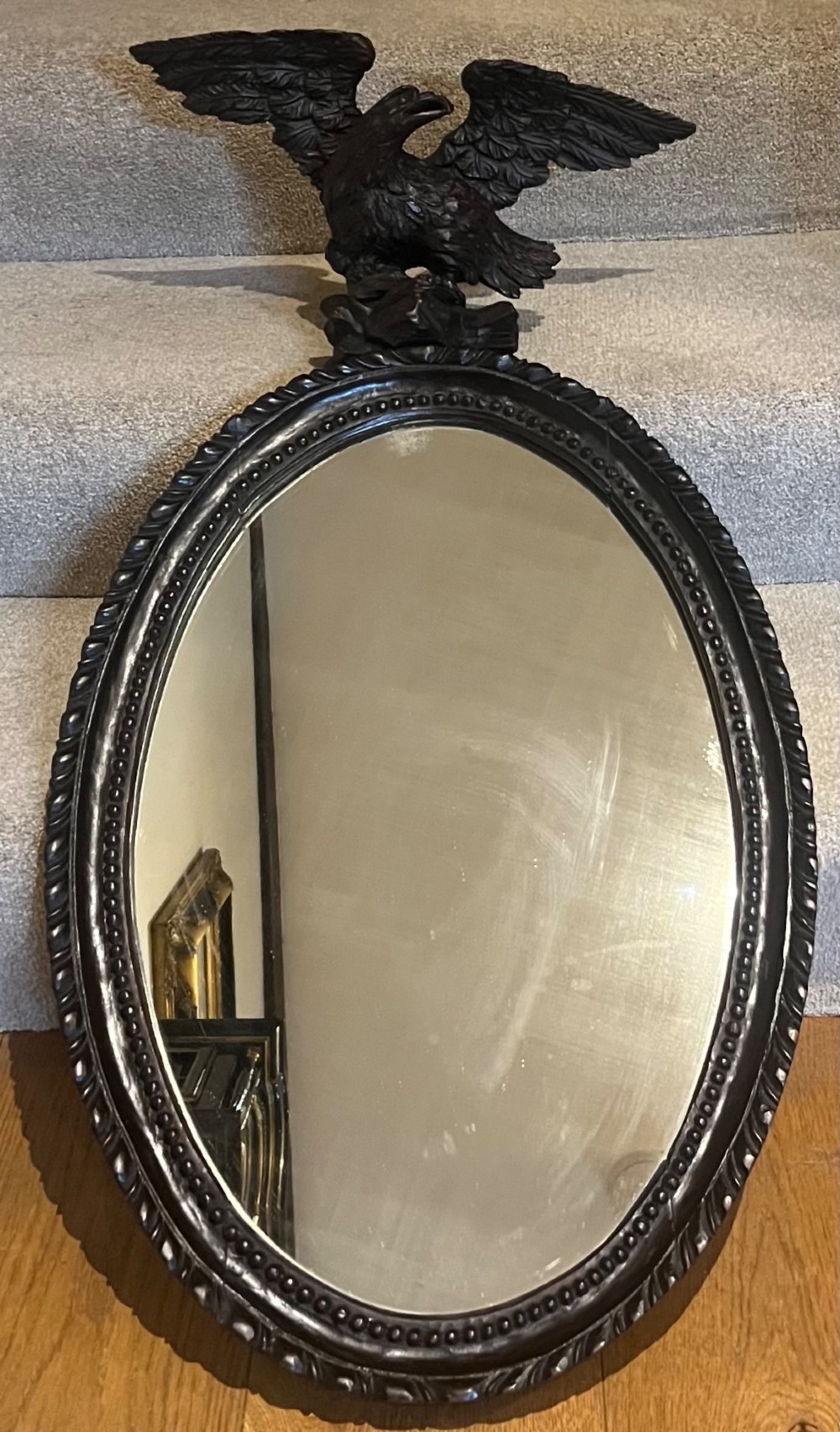 A dark stained oval wooden wall mirror featuring a carved eagle with spread wings perched atop a frame decorated with beaded and rope-twist detailing.