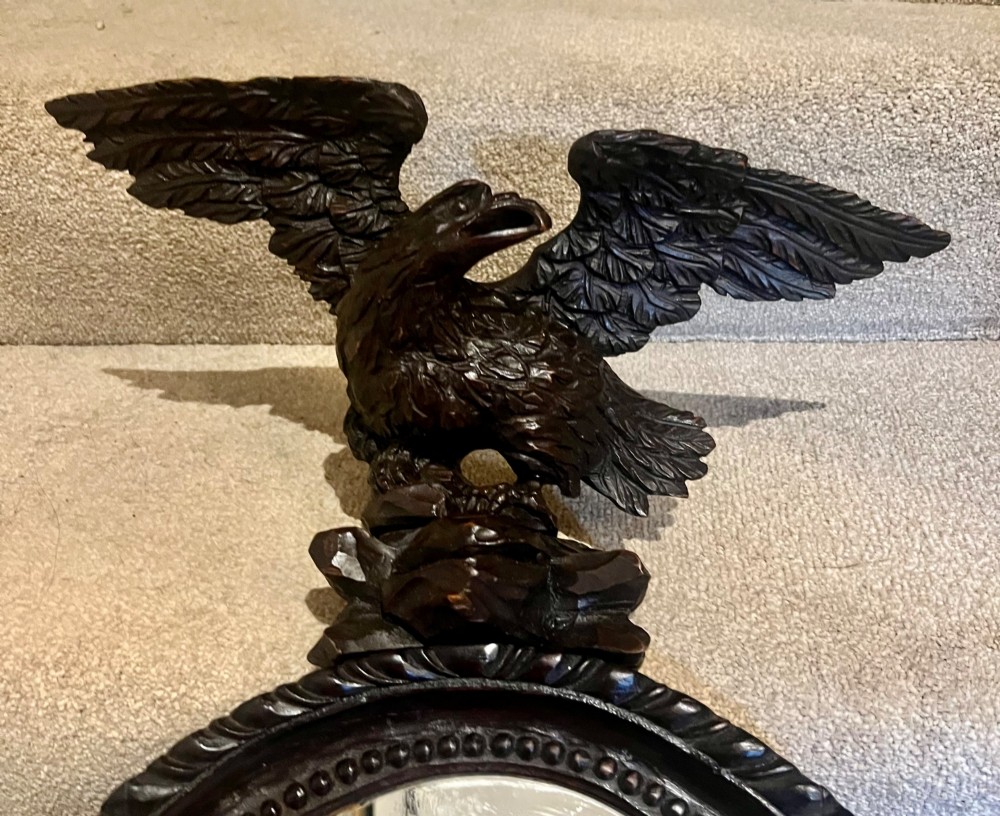 A dark stained oval wooden wall mirror featuring a carved eagle with spread wings perched atop a frame decorated with beaded and rope-twist detailing. View II