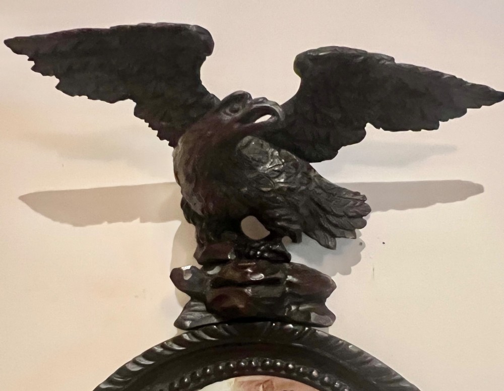 A dark stained oval wooden wall mirror featuring a carved eagle with spread wings perched atop a frame decorated with beaded and rope-twist detailing. View IX