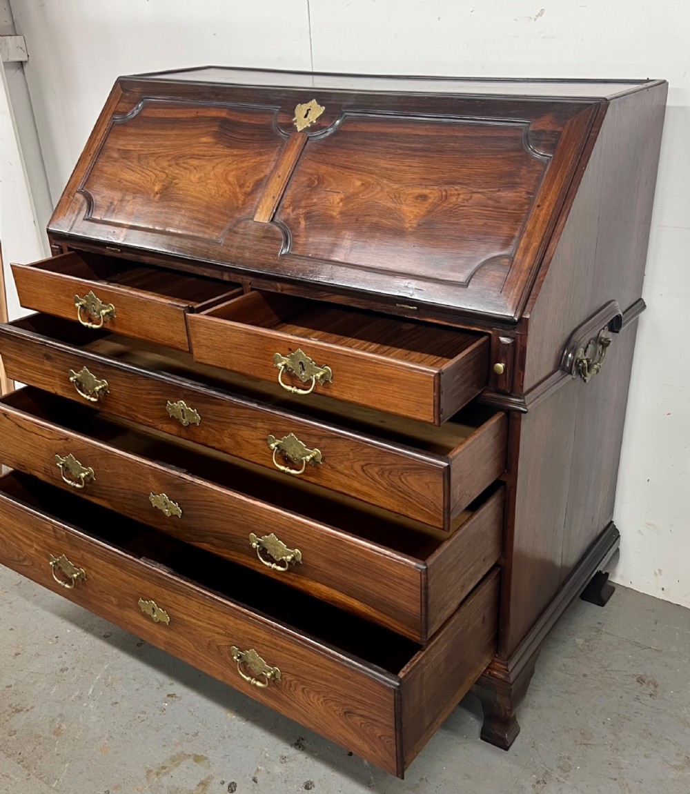 An 18th-century dark rosewood slant-front bureau shown open, featuring a stepped fitted interior, brass drop handles, and three long drawers below. View III