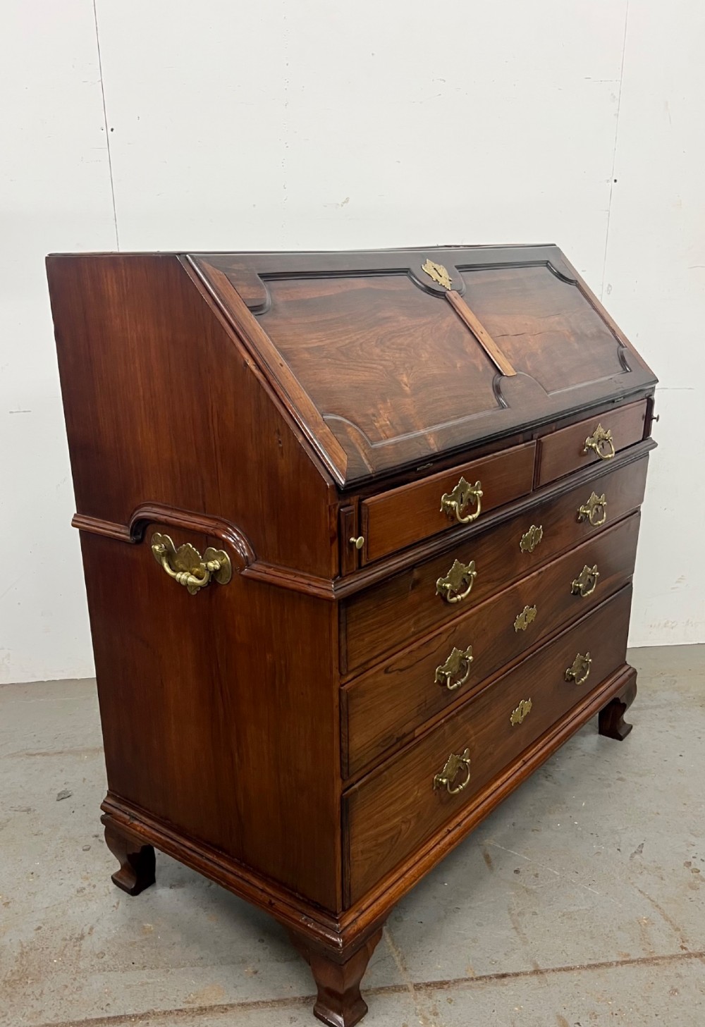 An 18th-century dark rosewood slant-front bureau shown open, featuring a stepped fitted interior, brass drop handles, and three long drawers below. View V