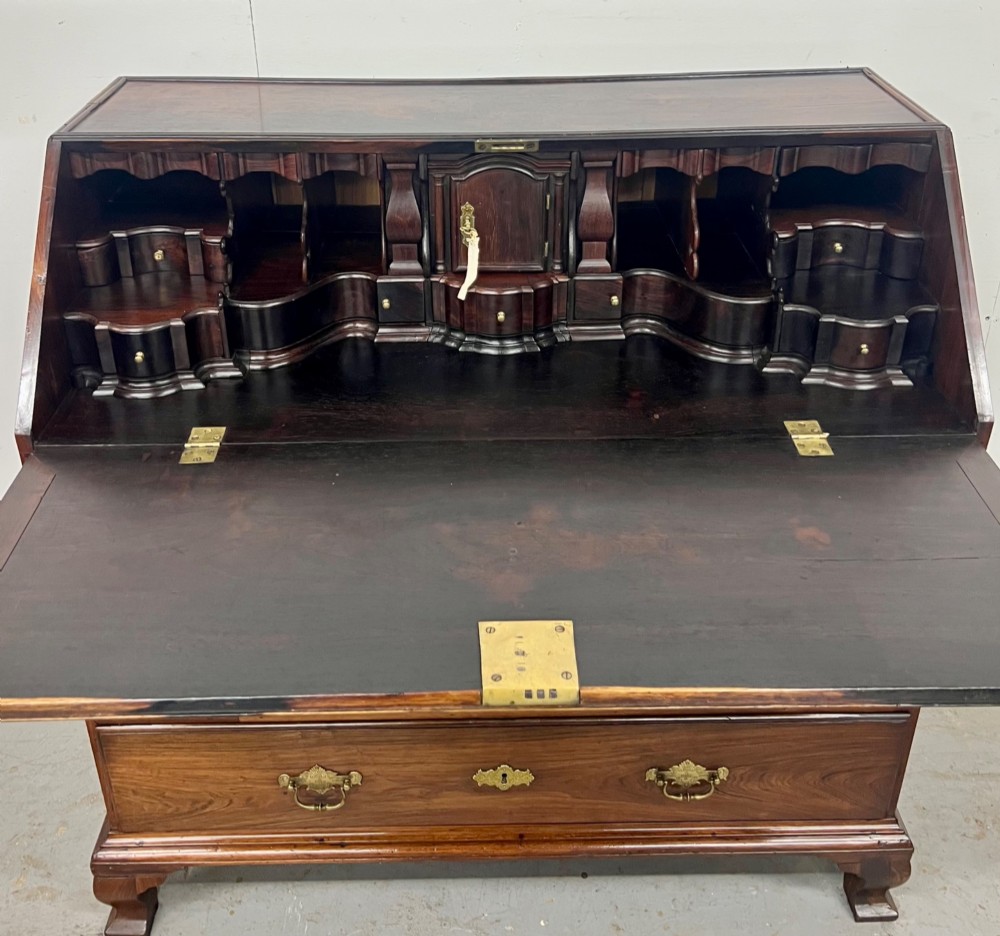 An 18th-century dark rosewood slant-front bureau shown open, featuring a stepped fitted interior, brass drop handles, and three long drawers below. View VIII