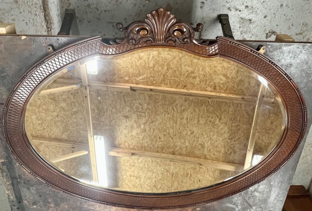 A large horizontal oval wall mirror with a dark carved wood frame featuring a central shell crest and cross-hatched border pattern.