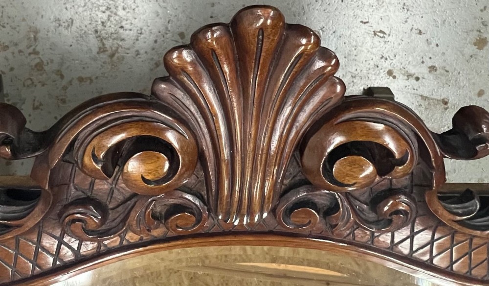 A large horizontal oval wall mirror with a dark carved wood frame featuring a central shell crest and cross-hatched border pattern. View III