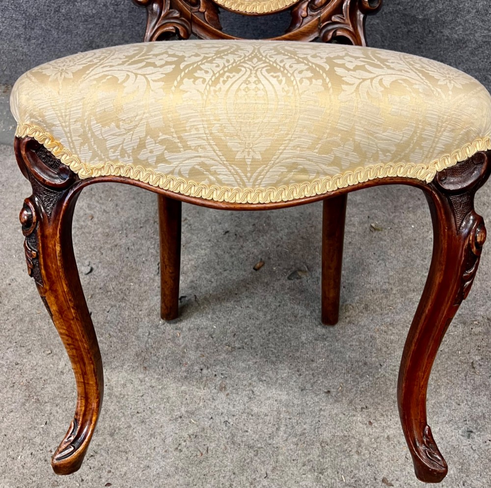 A set of six Victorian carved walnut dining chairs featuring oval balloon backs, cream patterned damask upholstery, and cabriole legs. View IV
