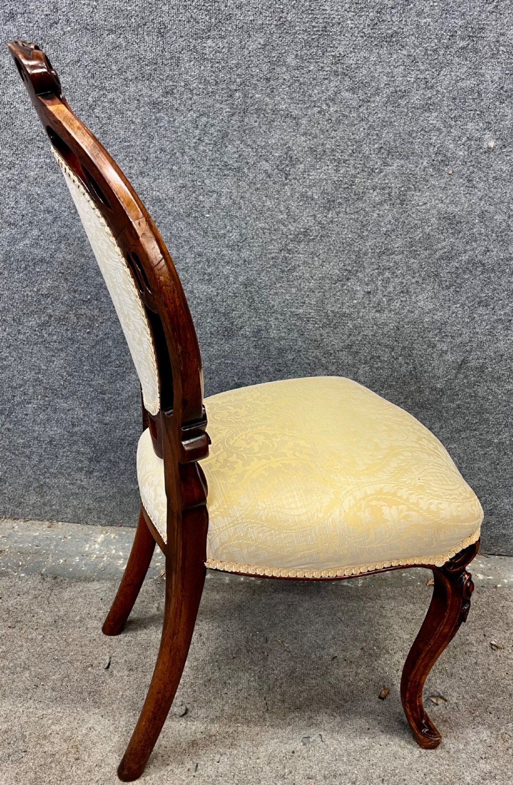 A set of six Victorian carved walnut dining chairs featuring oval balloon backs, cream patterned damask upholstery, and cabriole legs. View V