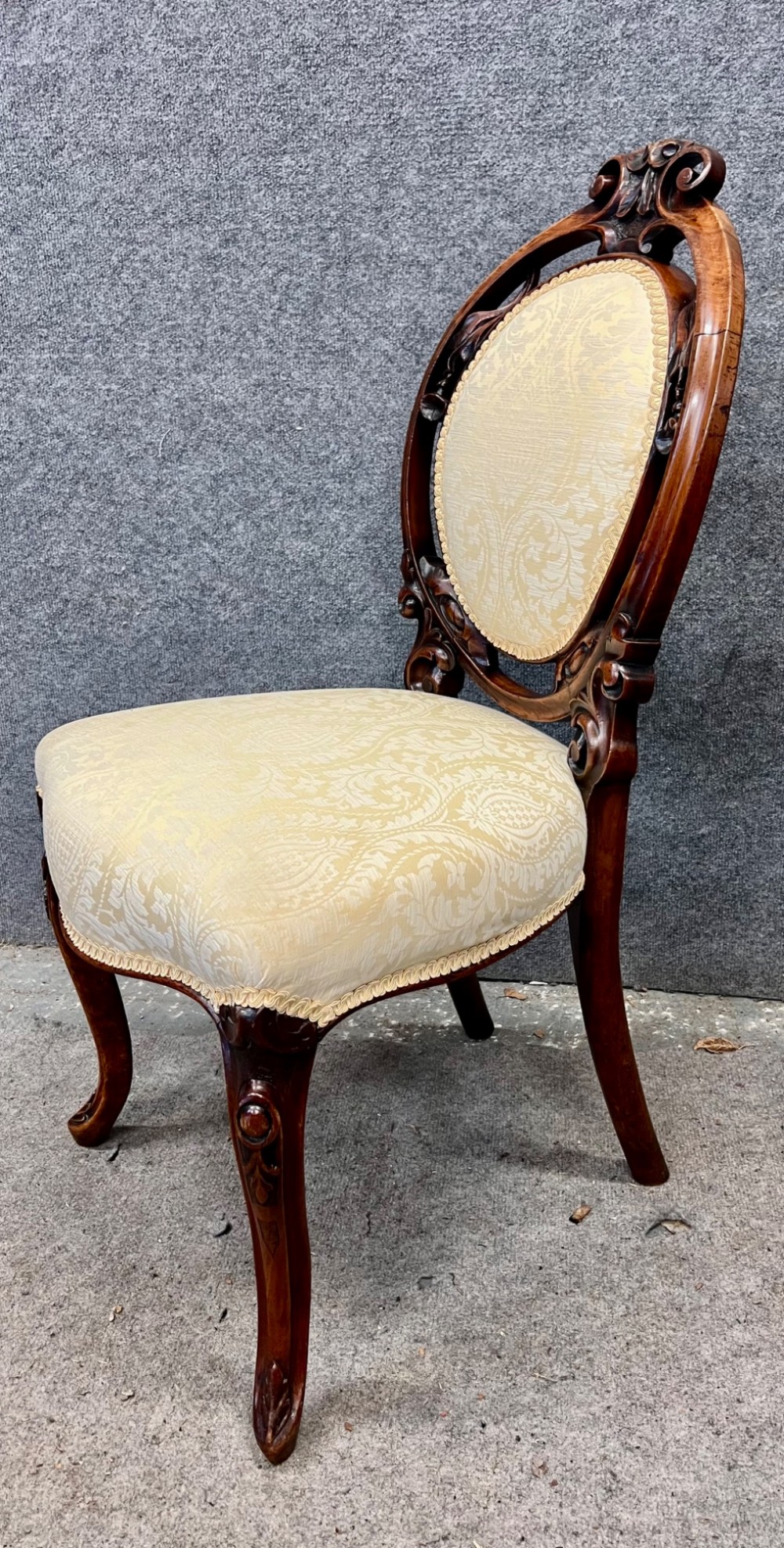 A set of six Victorian carved walnut dining chairs featuring oval balloon backs, cream patterned damask upholstery, and cabriole legs. View VII