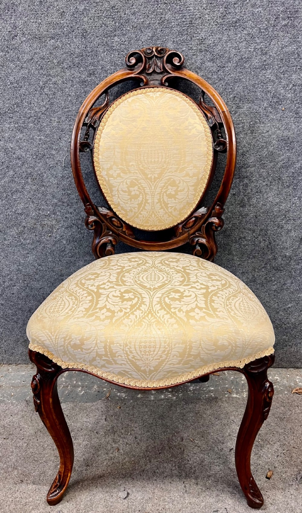 A set of six Victorian carved walnut dining chairs featuring oval balloon backs, cream patterned damask upholstery, and cabriole legs. View VIII