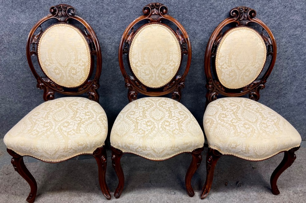 A set of six Victorian carved walnut dining chairs featuring oval balloon backs, cream patterned damask upholstery, and cabriole legs. View X
