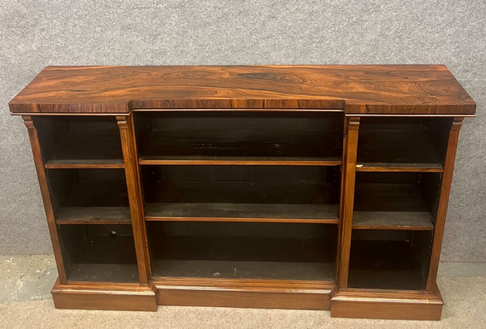 A low, wide Late Regency open rosewood bookcase featuring a breakfront top, three divided shelving sections, and a solid plinth base.