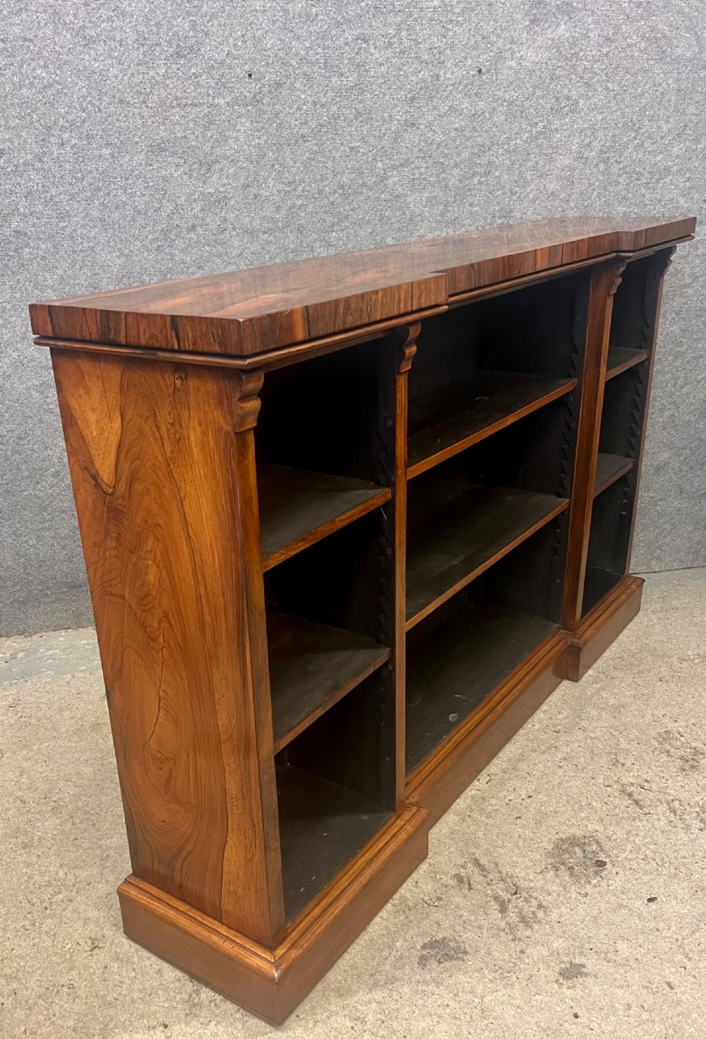 A low, wide Late Regency open rosewood bookcase featuring a breakfront top, three divided shelving sections, and a solid plinth base. View II