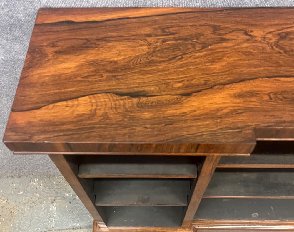A low, wide Late Regency open rosewood bookcase featuring a breakfront top, three divided shelving sections, and a solid plinth base. View VII