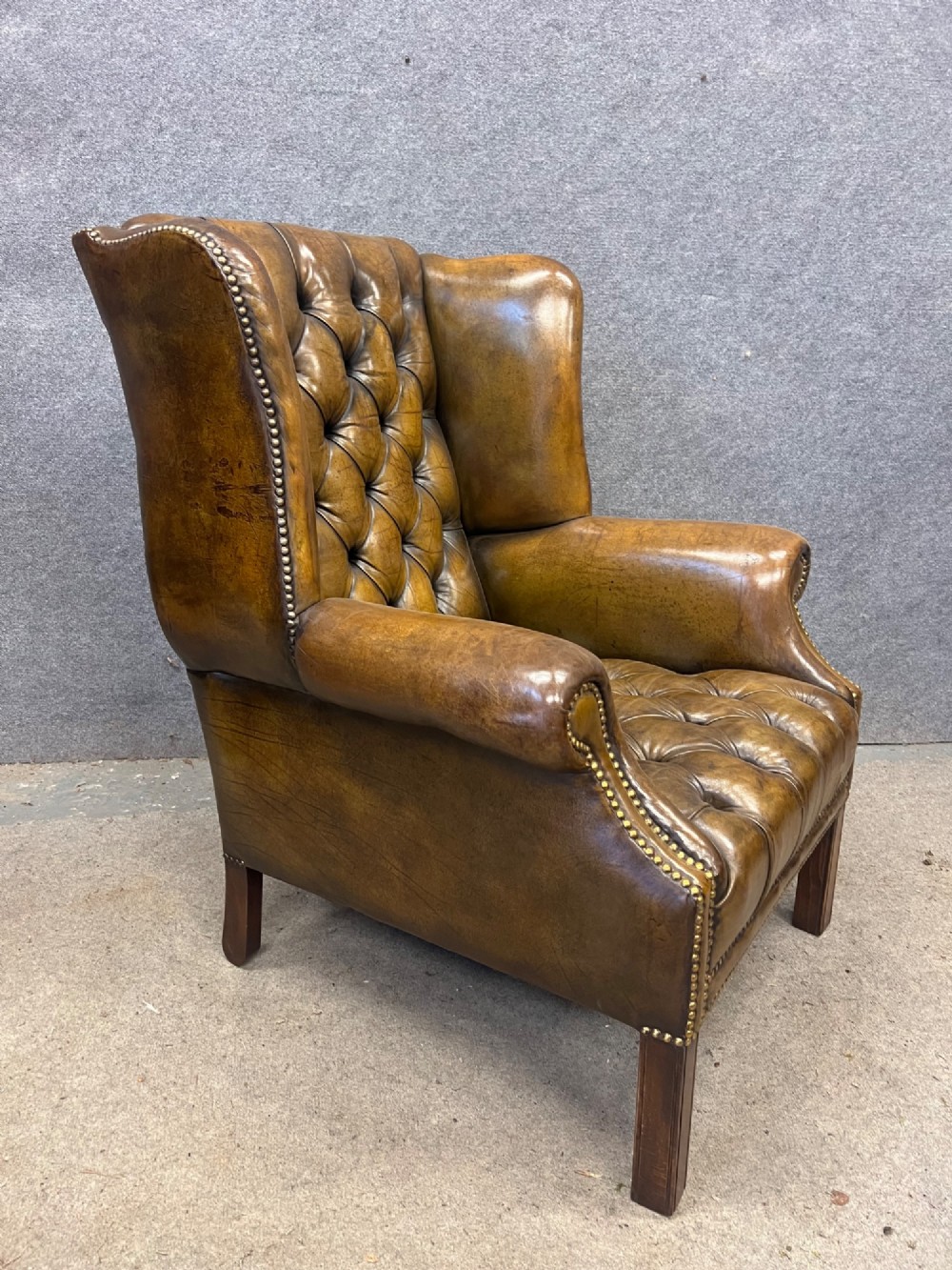A Georgian style brown leather wingback armchair featuring deep buttoned tufting, rolled arms, brass stud detailing, and square wooden legs. View II