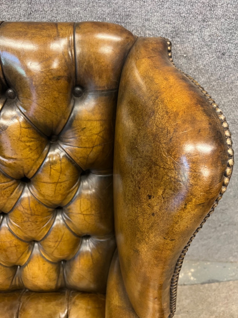 A Georgian style brown leather wingback armchair featuring deep buttoned tufting, rolled arms, brass stud detailing, and square wooden legs. View III