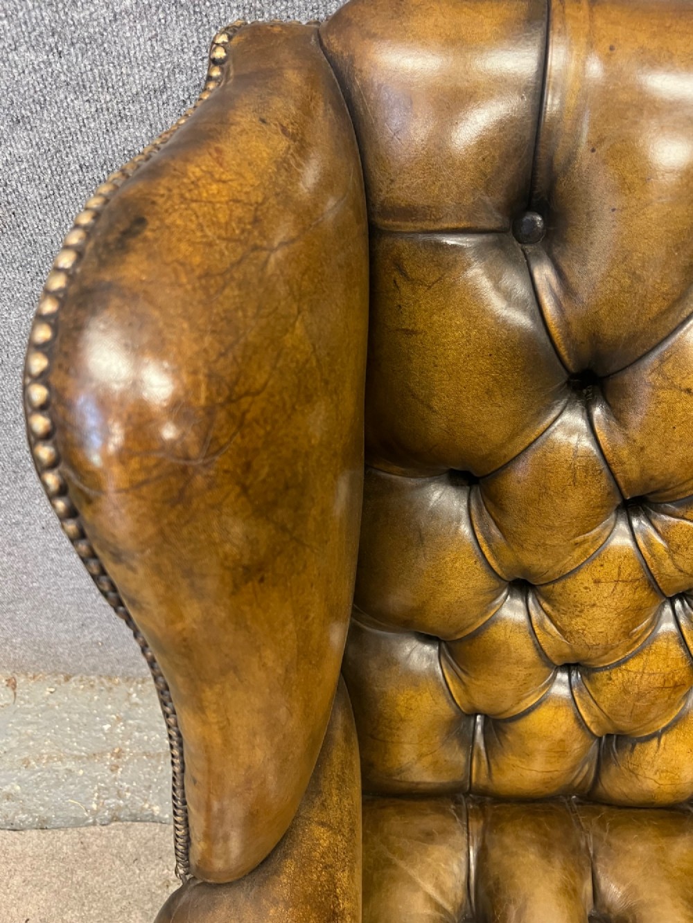 A Georgian style brown leather wingback armchair featuring deep buttoned tufting, rolled arms, brass stud detailing, and square wooden legs. View IV