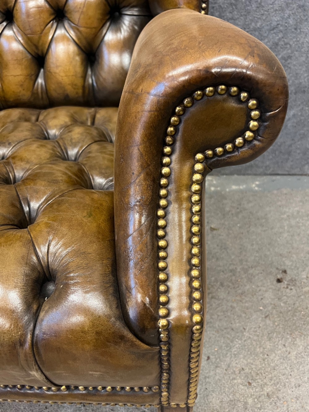 A Georgian style brown leather wingback armchair featuring deep buttoned tufting, rolled arms, brass stud detailing, and square wooden legs. View V