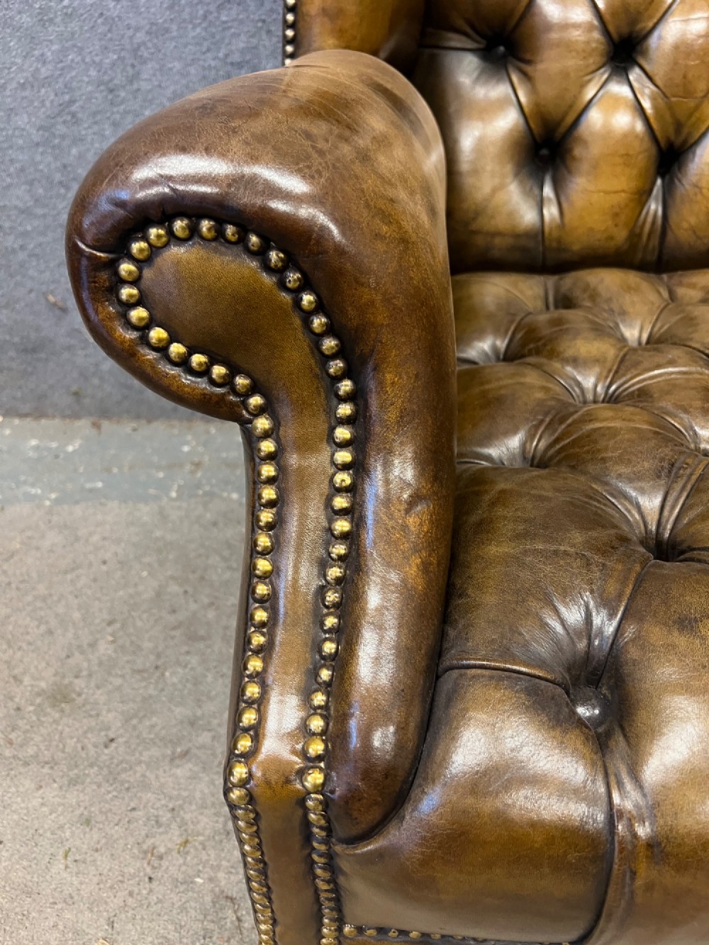 A Georgian style brown leather wingback armchair featuring deep buttoned tufting, rolled arms, brass stud detailing, and square wooden legs. View VI