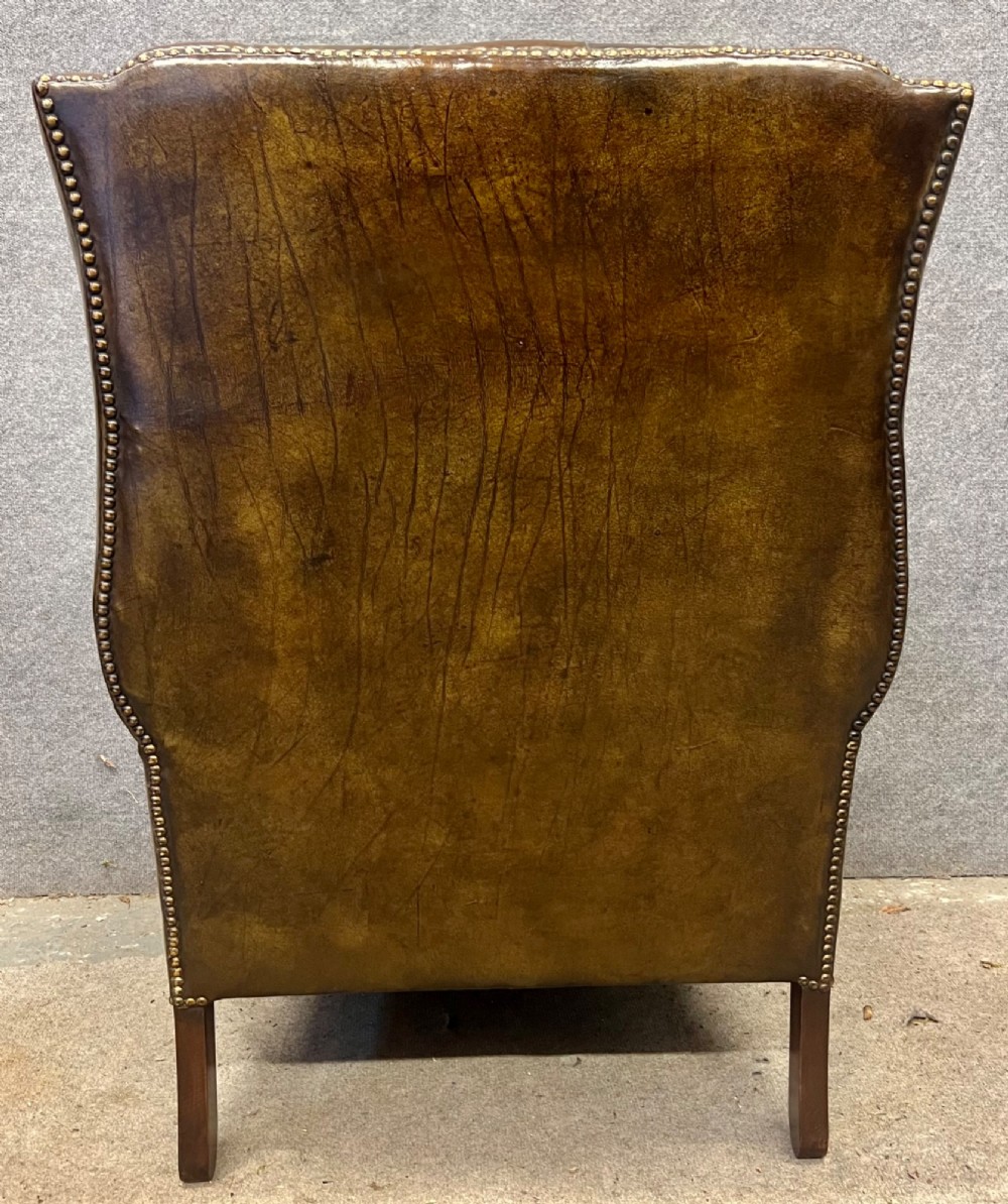 A Georgian style brown leather wingback armchair featuring deep buttoned tufting, rolled arms, brass stud detailing, and square wooden legs. View VIII