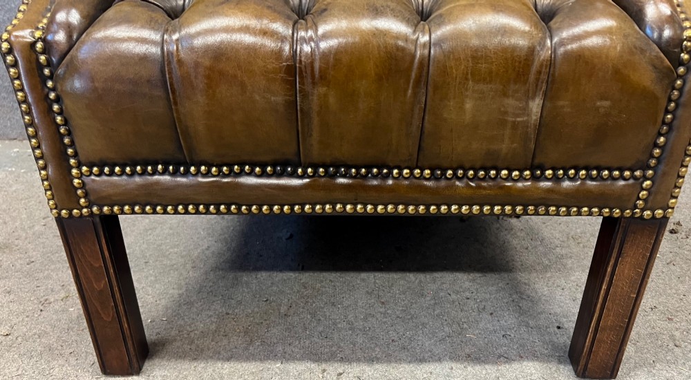 A Georgian style brown leather wingback armchair featuring deep buttoned tufting, rolled arms, brass stud detailing, and square wooden legs. View X