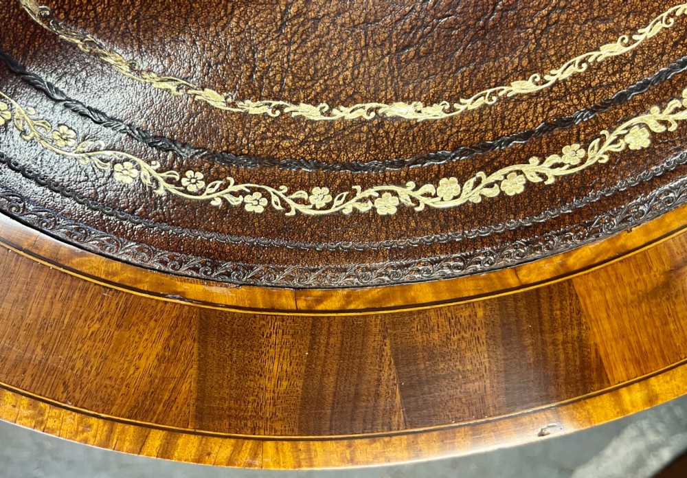 An Edwardian mahogany kidney-shaped desk featuring detailed floral marquetry inlay, a tooled leather writing surface, multiple drawers, and brass castors. View IX