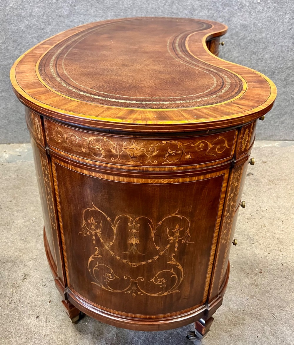 An Edwardian mahogany kidney-shaped desk featuring detailed floral marquetry inlay, a tooled leather writing surface, multiple drawers, and brass castors. View XII