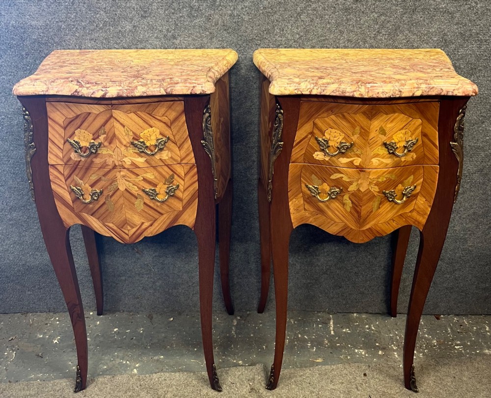 A pair of French Louis XV style bedside chests featuring floral marquetry inlay, curved cabriole legs, decorative metal mounts, and shaped pink marble tops.