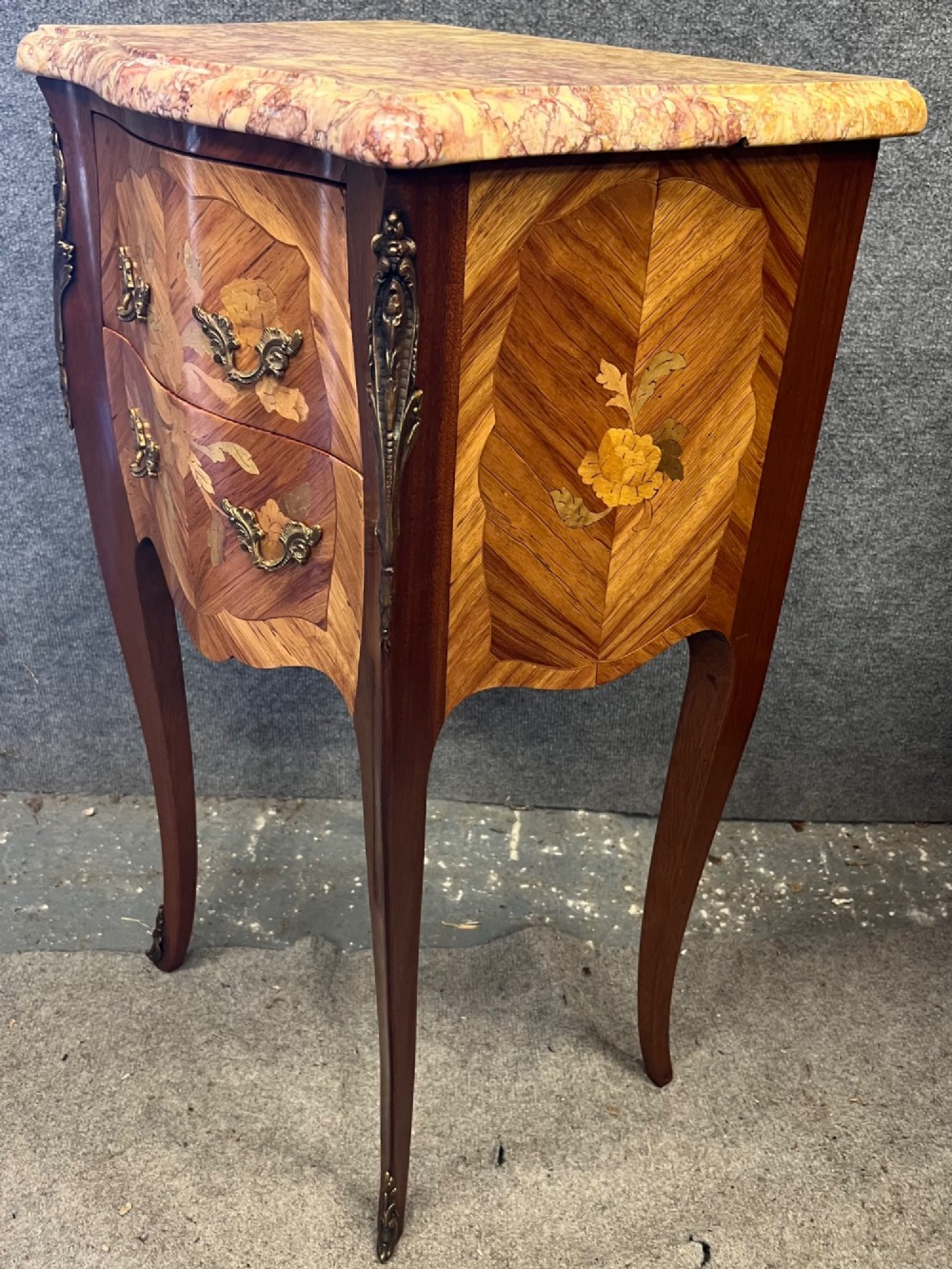 A pair of French Louis XV style bedside chests featuring floral marquetry inlay, curved cabriole legs, decorative metal mounts, and shaped pink marble tops. View IV