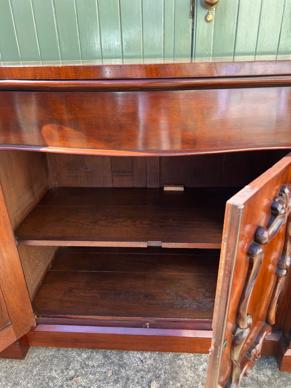 A nineteenth-century mahogany sideboard featuring a large carved mirror frame upstand, central double cupboard doors, flanking side doors with scroll mouldings, and flame timber veneers. View XIV